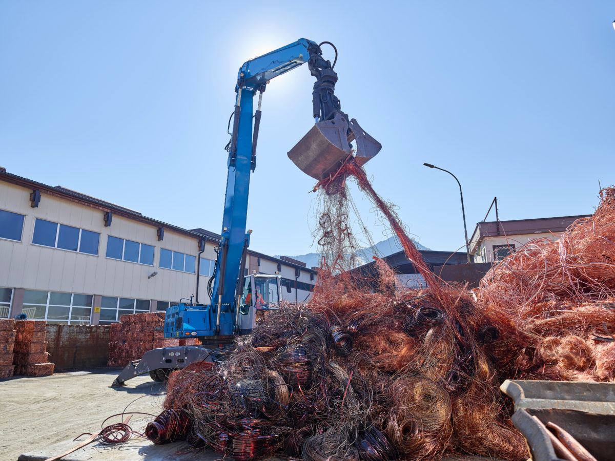 Grue hydraulique bleue manipulant des fils de cuivre emmêlés sur site de recyclage industriel